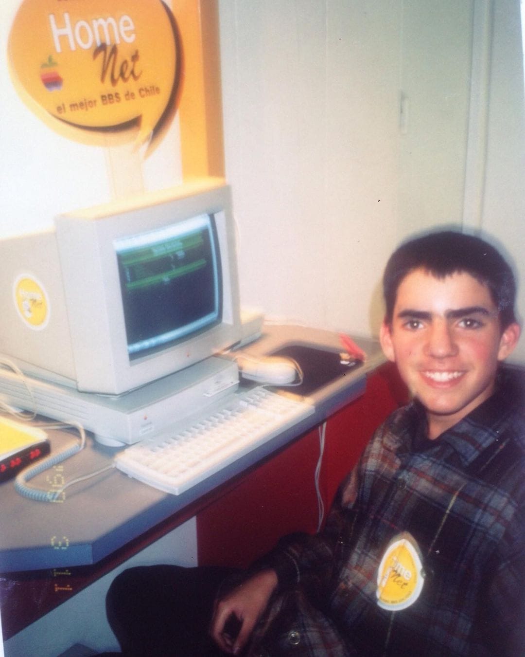 Leo Prieto a los 14 años frente a un computador Macintosh de 1994, con un modem conectado a un BBS que se ve en el terminal en su pantalla.